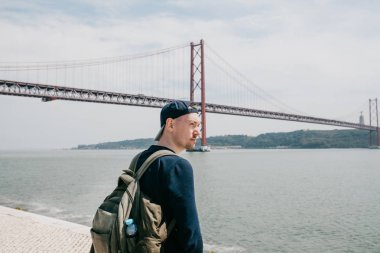 Genç bir seyahat veya bir turist Lizbon Portekiz Waterfront 25 Nisan köprünün yanındaki bir sırt çantası ile