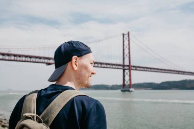 Genç bir seyahat veya bir turist Lizbon Portekiz Waterfront 25 Nisan köprünün yanındaki bir sırt çantası ile