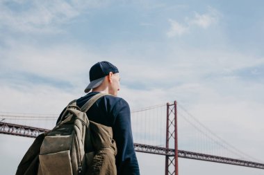 Genç bir seyahat veya bir turist Lizbon Portekiz Waterfront 25 Nisan köprünün yanındaki bir sırt çantası ile