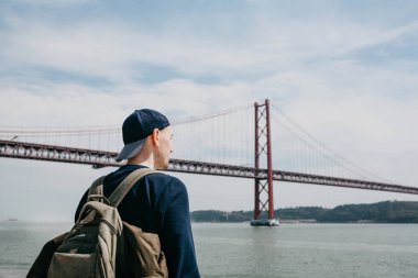 Genç bir seyahat veya bir turist Lizbon Portekiz Waterfront 25 Nisan köprünün yanındaki bir sırt çantası ile