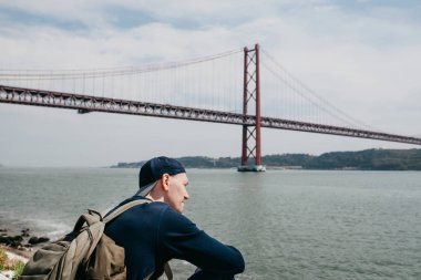 Genç bir seyahat veya bir turist Lizbon Portekiz Waterfront 25 Nisan köprünün yanındaki bir sırt çantası ile
