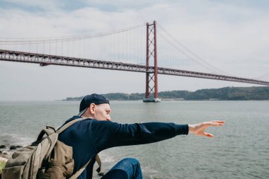 Genç bir seyahat veya bir turist Lizbon Portekiz Waterfront 25 Nisan köprünün yanındaki bir sırt çantası ile