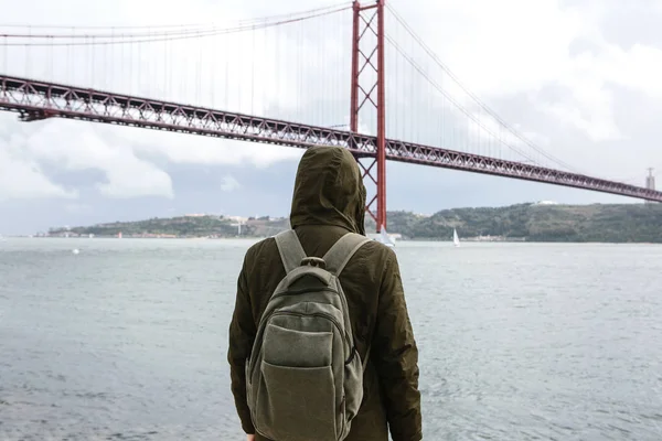 Genç bir seyahat veya bir turist Lizbon Portekiz Waterfront 25 Nisan köprünün yanındaki bir sırt çantası ile