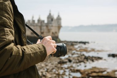 Profesyonel bir fotoğrafçı ya da bir genç erkek turist fotoğrafları Lizbon Portekiz manzaraları. Bir kamera tutar. Torre de Belem görünürde arka plan bulanık.