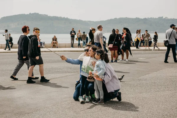 Portugal, Lisbon, May 1, 2018: A young Asian family father, mother and two daughters make an emotional selfie on the waterfront in Belem. People are walking around — Stock Photo, Image