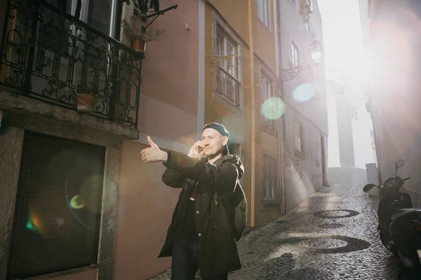 Portekiz'de Lizbon sokakta bir sırt çantası ile telefonda konuşurken ve eliyle bir işaret gösteren genç adam Turizm