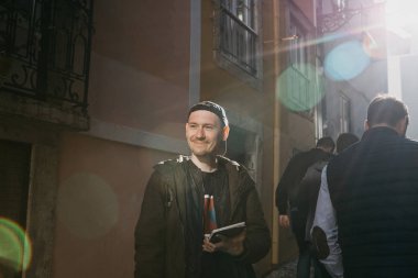 Sokakta bir tablet gülümseyen genç erkek turist. İnsanlar tarafından yürüyor