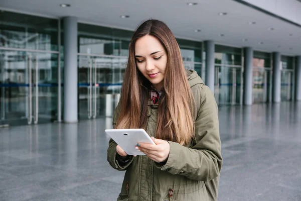 Una mujer joven y hermosa usa una tableta para comunicarse con sus amigos o mira un mapa o llama a un taxi u otra cosa. — Foto de Stock