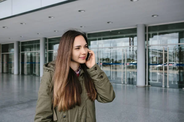 Joven chica hermosa turística en el aeropuerto o cerca del centro comercial o la estación llama a un taxi o hablar por teléfono celular o hablar con amigos usando un teléfono móvil — Foto de Stock