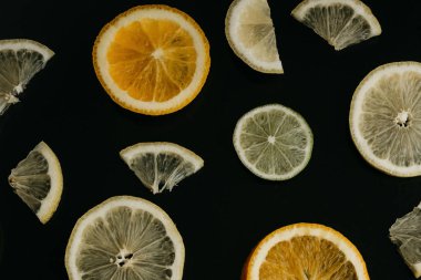 Siyah bir zemin üzerine narenciye. Birçok dilim limon, portakal ve limon birlikte yalan. Bir sürü meyve. Sağlıklı yemek ve vitaminler