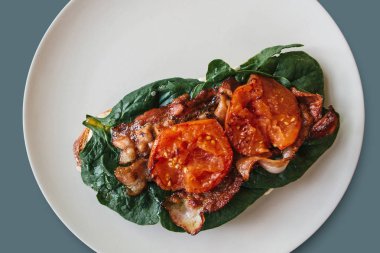 Yakın çekim. Lezzetli ve besleyici tost ya da sandviç sosis, ıspanak ve domates üzerinde gri bir arka plan ile. Lezzetli yemekler