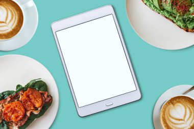 Yukarıdan görüntüleyin. Bir tablet metin için boş bir ekran ile ortada. Onun yanında çeşitli yemek ve kahve. Online yemek siparişi gıda teslim ya da rahat bir sabah.