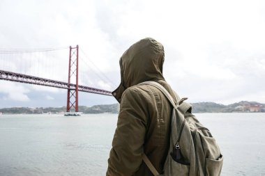 Genç bir seyahat veya bir turist Lizbon Portekiz Waterfront 25 Nisan köprünün yanındaki bir sırt çantası ile
