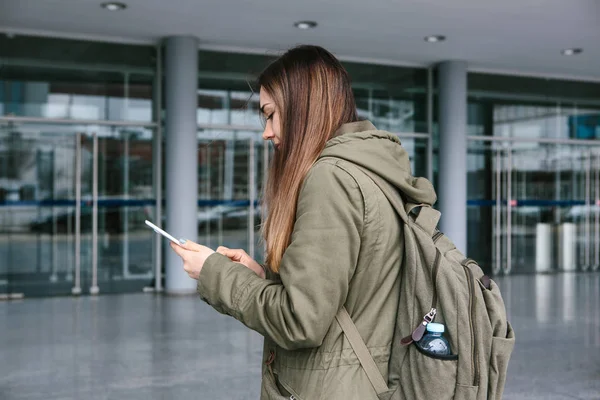 Una mujer joven y hermosa usa una tableta para comunicarse con sus amigos o mira un mapa o llama a un taxi u otra cosa. — Foto de Stock