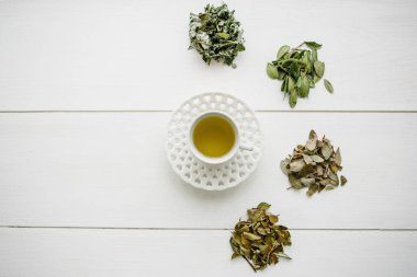 Taze kokulu ve sağlıklı bitki çayı bir cam veya kupa bir beyaz tahta yüzey üzerinde. Yanında çay yapmak için çeşitli kuru otlar yalan. Sağlıklı ürün