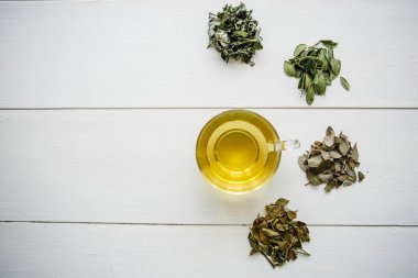 Taze kokulu ve sağlıklı bitki çayı bir cam veya kupa bir beyaz tahta yüzey üzerinde. Yanında çay yapmak için çeşitli kuru otlar yalan. Sağlıklı ürün