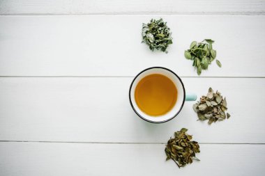 Taze kokulu ve sağlıklı bitki çayı bir cam veya kupa bir beyaz tahta yüzey üzerinde. Yanında çay yapmak için çeşitli kuru otlar yalan. Sağlıklı ürün