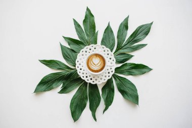 Lezzetli taze sabah cappuccino bir çiçek desenli bir kupa kahve. Dekorasyon için bitki yaprakları yakın yalan