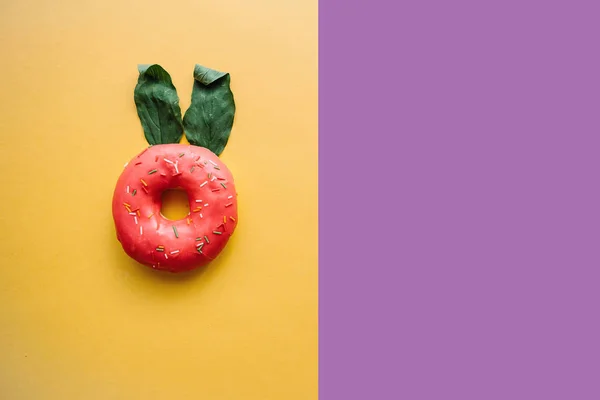 Un donut creativo con orejas de hojas que se asemejan a un conejo sobre un fondo de color en un estilo minimalista. Lugar cercano para el texto — Foto de Stock