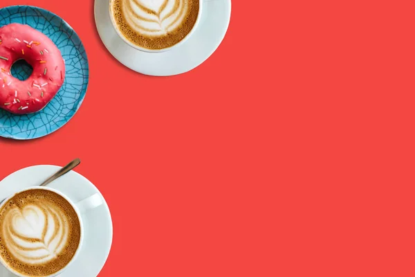 Dos tazas de delicioso café cappuccino fragante y una serie de rosquillas sobre un fondo rojo. Lugar cercano para el texto . — Foto de Stock
