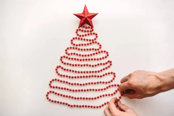 Una persona fa un albero di Natale o Capodanno creativo fatto di perline in stile minimalista e decora con una stella. . — Foto Stock