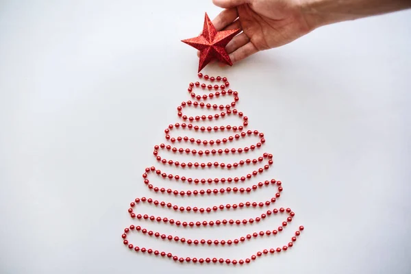 Una persona fa un albero di Natale o Capodanno creativo fatto di perline in stile minimalista e decora con una stella. . — Foto Stock