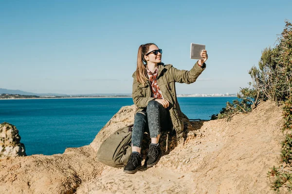 Una joven hermosa chica hace selfie o habla mediante el uso de una tableta en línea o toma fotos de un hermoso paisaje — Foto de Stock