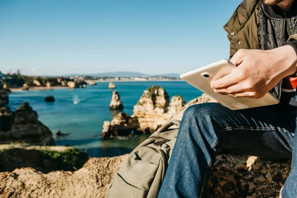 Un tânăr sau un turist folosește o tabletă așezată pe coasta Atlanticului — Fotografie, imagine de stoc