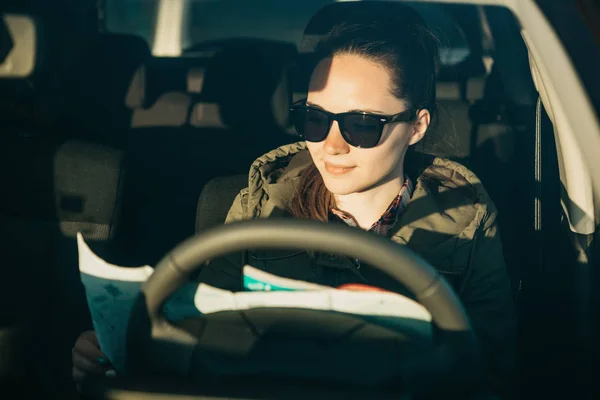 Retrato de una joven turista o conductora dentro de un coche que mira el mapa para un viaje posterior . — Foto de Stock