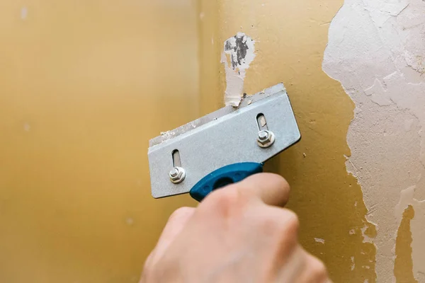 Ein Mann mit einem Schaber entfernt die alte Verkleidung von der Wand. — Stockfoto