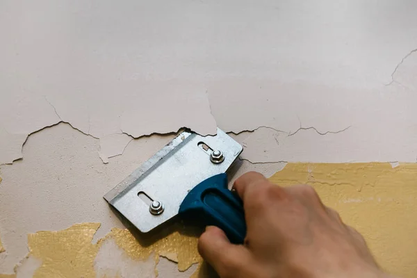 Ein Mann mit einem Schaber entfernt die alte Verkleidung von der Wand. — Stockfoto