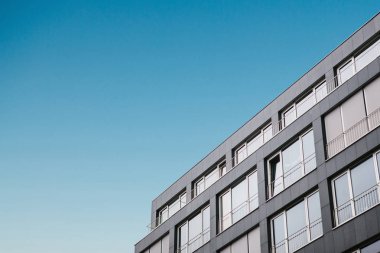 Mavi gökyüzüne karşı bir minimalist tarzda birçok windows ile bina köşesi.