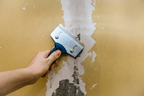 Ein Mann mit einem Schaber entfernt die alte Verkleidung von der Wand. — Stockfoto