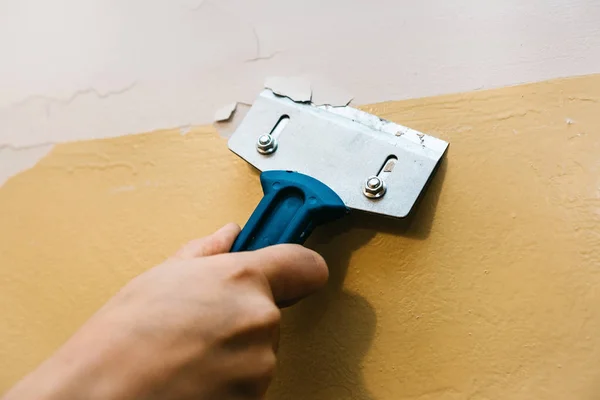 Ein Mann mit einem Schaber entfernt die alte Verkleidung von der Wand. — Stockfoto