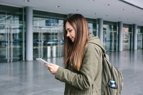 Una mujer joven y hermosa usa una tableta para comunicarse con sus amigos o mira un mapa o llama a un taxi u otra cosa. — Foto de Stock