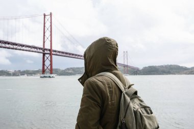 Genç bir seyahat veya bir turist Lizbon Portekiz Waterfront 25 Nisan köprünün yanındaki bir sırt çantası ile