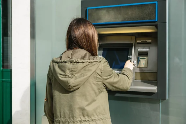 Una mujer joven toma dinero de un cajero automático. Toma una tarjeta del cajero automático. Finanzas, tarjeta de crédito, retiro de dinero . — Foto de Stock