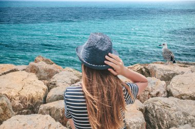 Şapkalı bir kız güzel bir manzara okyanus veya deniz kıyısında oturan keyif alıyor