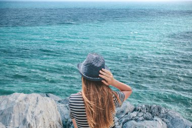 Şapkalı bir kız güzel bir manzara okyanus veya deniz kıyısında oturan keyif alıyor