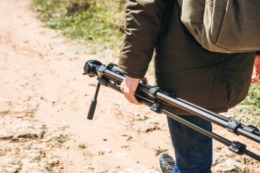 Bir fotoğrafçı, kameraman ya da gezgin bir sırt çantası ve tripod elinde dağlık arazi yürüyor.