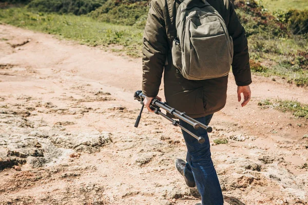 Ein Fotograf oder Videograf oder ein Reisender mit Rucksack und Stativ in der Hand spaziert durch das bergige Gelände. — Stockfoto