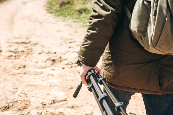 Bir fotoğrafçı, kameraman ya da gezgin bir sırt çantası ve tripod elinde dağlık arazi yürüyor.