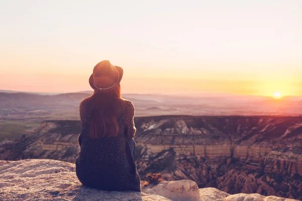 Uma vista da parte de trás de uma menina em um chapéu senta-se em uma colina e admira a bela vista . — Fotografia de Stock