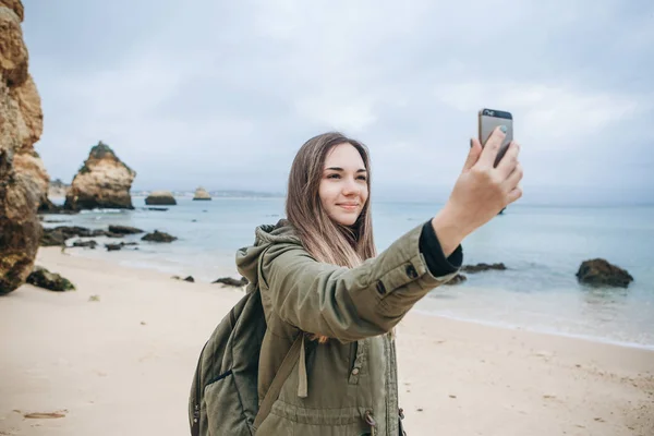 Una chica turística positiva toma una hermosa vista o hace una selfie o se comunica con alguien en línea utilizando un teléfono celular — Foto de Stock
