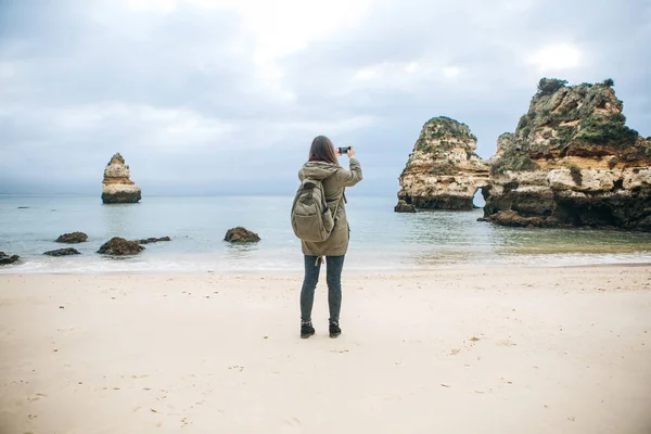 Chica turista con una mochila fotografiando un hermoso paisaje de pie en la costa atlántica — Foto de Stock