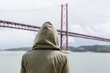 Arkadan görüntüleyin. Rüzgarlı havalarda başlıklı bir kız güzel bir köprü görünüm