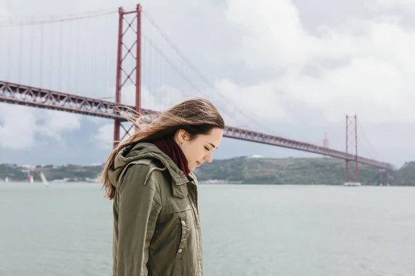 Una hermosa chica camina sola a lo largo de la orilla cerca del puente en Lisboa . — Foto de Stock