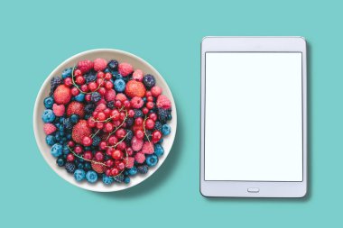 Yukarıdan görüntüleyin. Bir tabak içinde farklı meyveler. Tablet ile çeşitli bir beyaz perde.