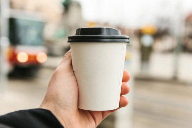 Genç bir adam kahve ya da başka bir sıcak içecek ile tek kullanımlık bir bardak soğuk sezonda tutar..