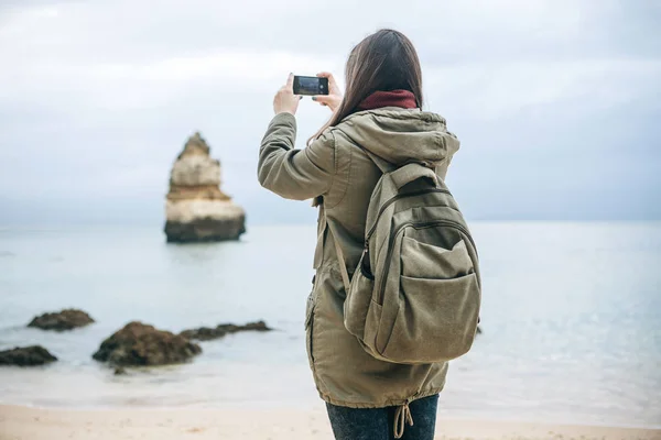 Chica turista con una mochila fotografiando un hermoso paisaje de pie en la costa atlántica — Foto de Stock